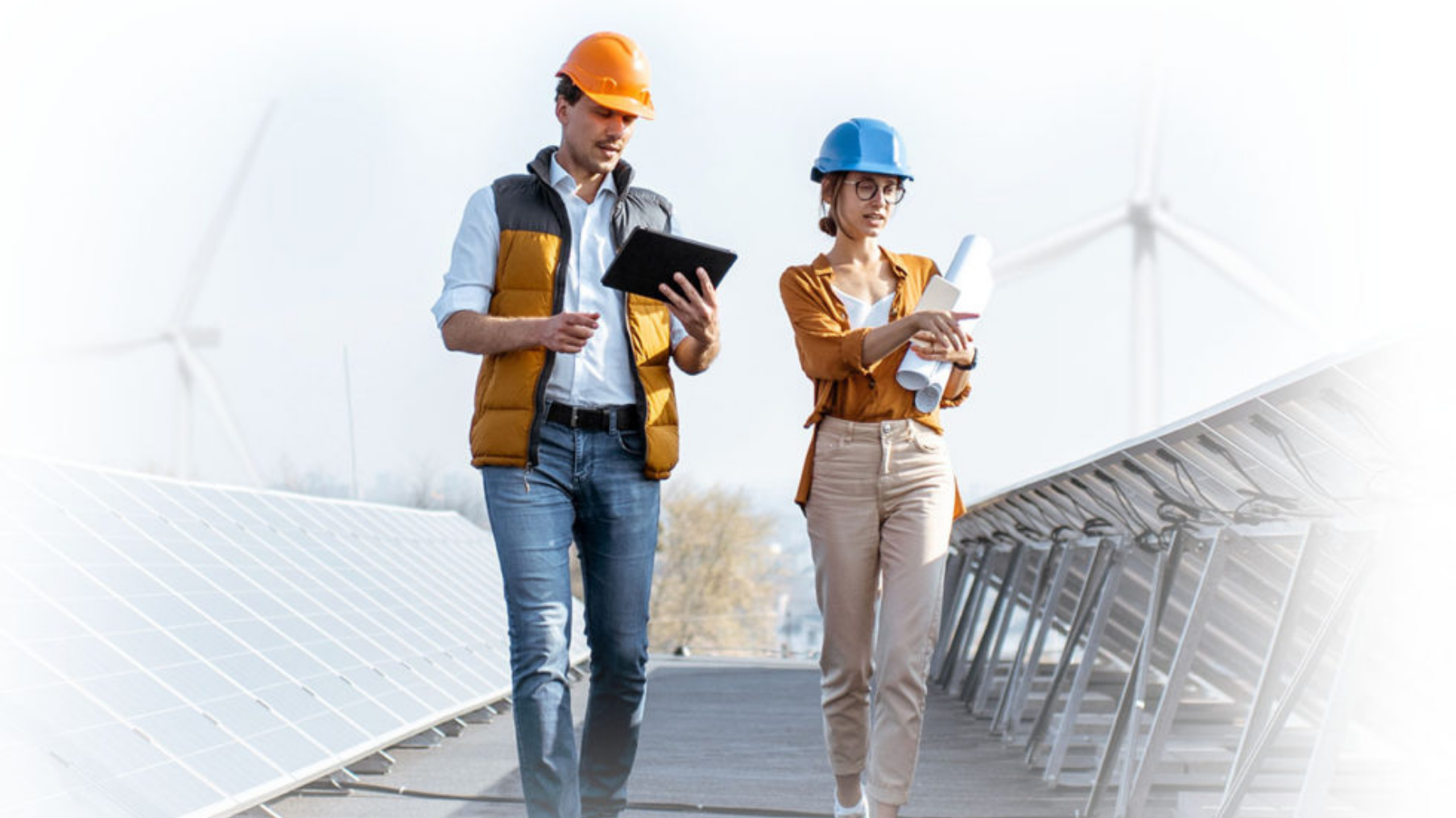 person writing in a notebook beside by an iPad, laptop, printed photos, spectacles, and a cup of coffee on a saucer